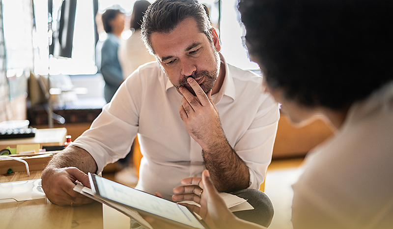 Ein konzentrierter Mitarbeiter sitzt am Tisch mit einer Mitarbeiterin. Sie werten ein Online Assessment aus.