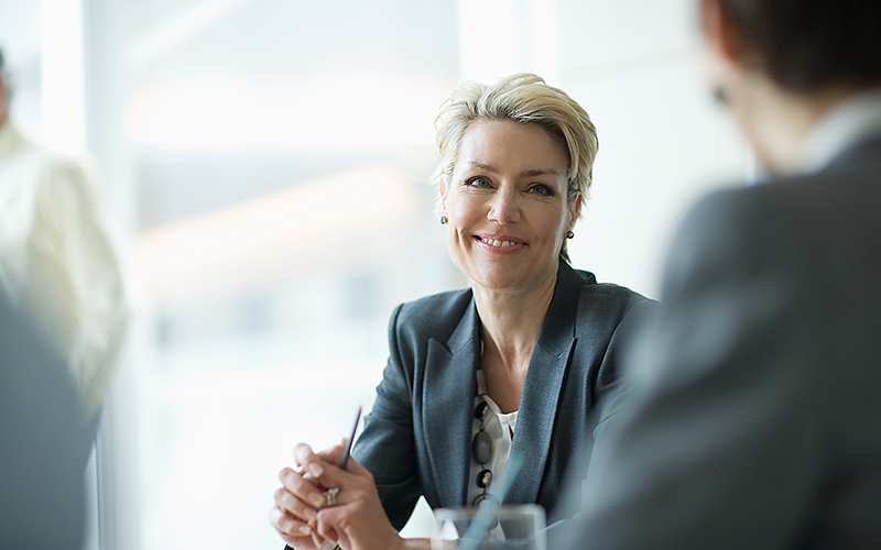 Eine erfolgreiche Geschäftsfrau im Business-Dress sitzt im Büro und diskutiert mit unserem Mitarbeiter über ihren Platz in der C-Suite.