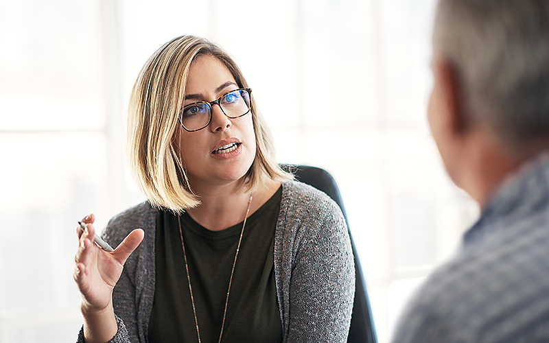 Eine blonde Mitarbeiterin sitzt im Büro und gibt einem Kunden ein Karriere-Coaching.